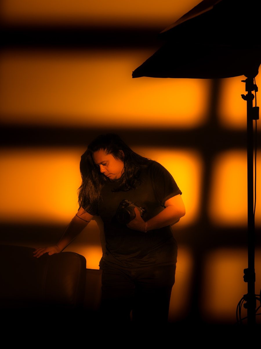 Teddy Forte holding a camera in a studio, lit by warm orange window light